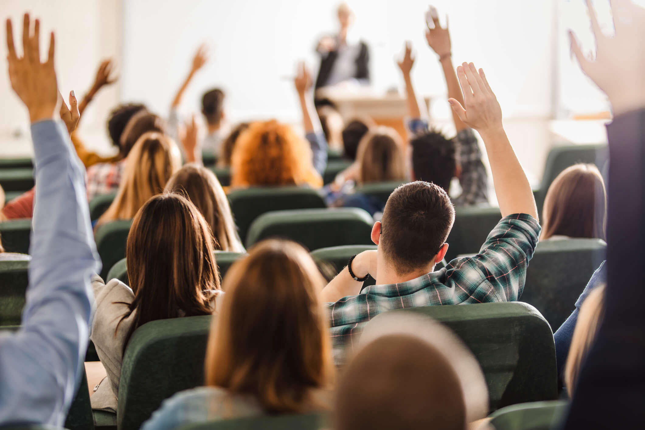 A group of peopel whith their hands in the air ready to ask a question